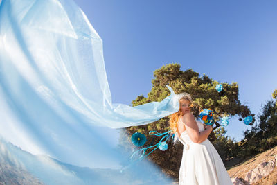 Young woman standing against blue sky