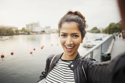 Portrait of smiling woman standing against river in city