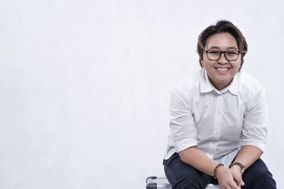 Portrait of woman smiling while sitting on seat against white background