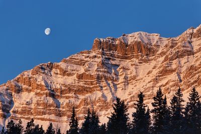 Low angle view of snowcapped mountains against clear blue sky