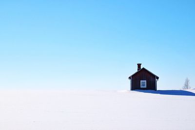 Low angle view of house on snow covered field against clear sky