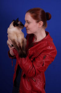 Young woman carrying cat while standing against blue background