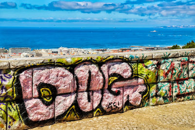 Graffiti on wall by sea against sky