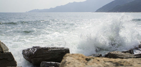 Waves splashing on rocks at shore against sky