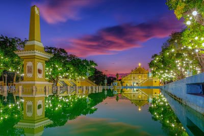 Illuminated building by lake against sky