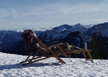 View of deck chair on snow covered land against sky