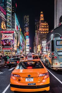 Yellow taxi on city street by illuminated buildings at night