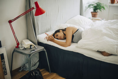 Woman checking blood sugar level while lying on bed in bedroom