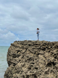 Woman standing on rock by sea against sky