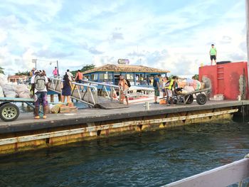 People at amusement park by river in city against sky