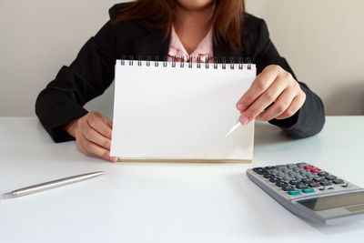 Midsection of businesswoman with spiral notebook on table