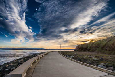 Road by sea against sky during sunset