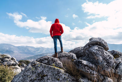 Unrecognizable man standing on the rocks on top of a mountain  under a blue sky with clouds