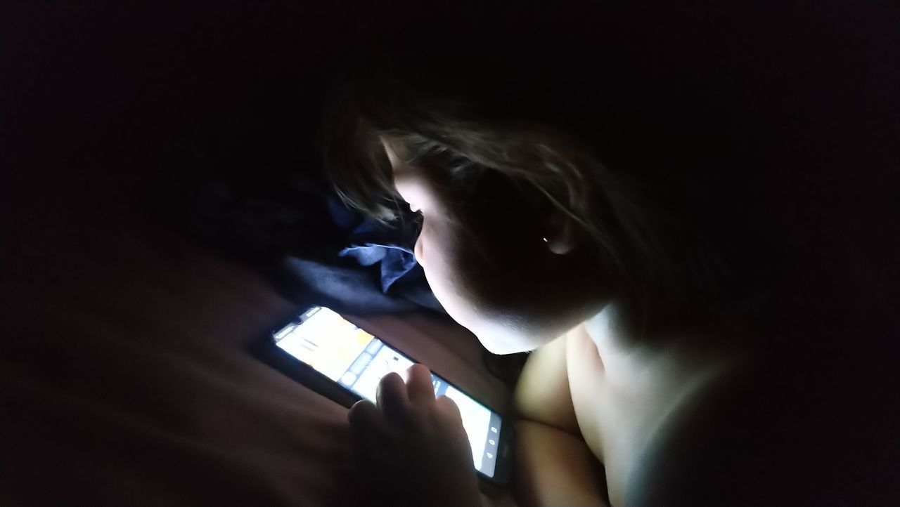 REAR VIEW OF WOMAN USING MOBILE PHONE IN DARK ROOM