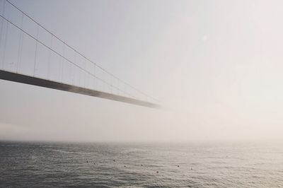 Suspension bridge over sea against clear sky