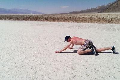 Full length of shirtless man kneeling on sand at desert