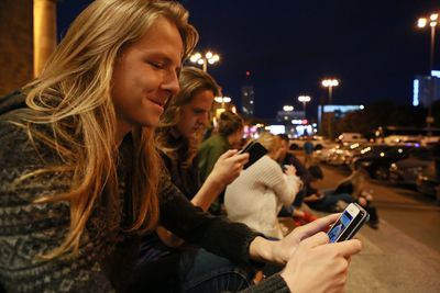 Women using mobile phones on steps in city at night