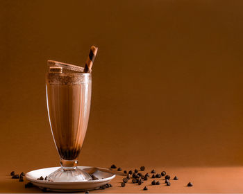 Close-up of chocolate milkshake in glass against brown background