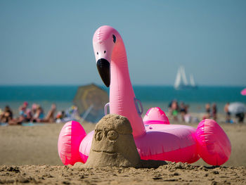 Beach scene during holidays with a sand minion and a inflatable flamingo in the foreground