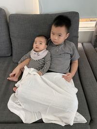 High angle view of cute brothers sitting on sofa