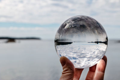 Cropped image of hand holding crystal ball against sky