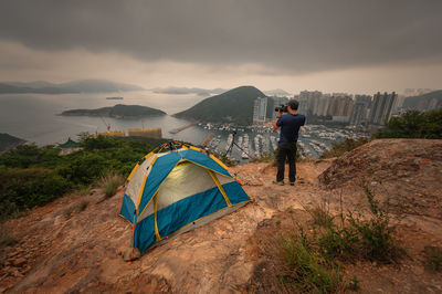 Man traveler taking photo on top of mountains near of tent camping