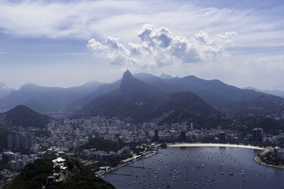 High angle view of city by river and mountains against sky