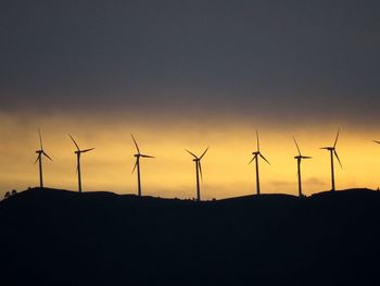 Silhouette wind turbines on field against sky during sunset