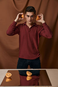 Portrait of a young man holding camera while standing on table