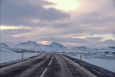 Road amidst snowcapped mountains against sky during winter