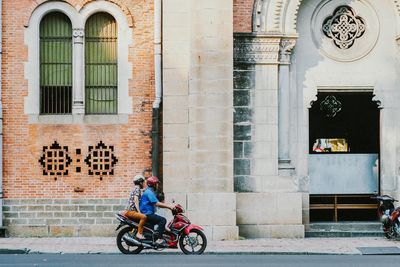 Three people riding moped on city street