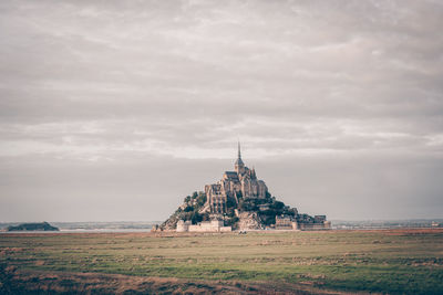 Building on field against cloudy sky