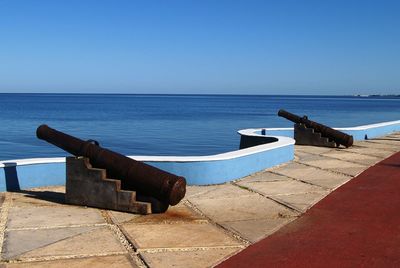 Cannons by sea against clear sky on sunny day