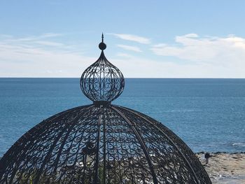 Metallic structure by sea against sky