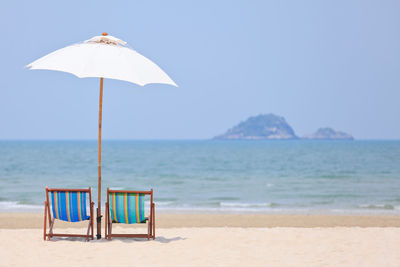 Deck chairs on beach against sky