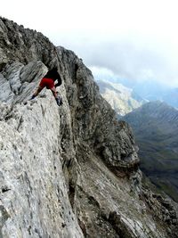 Low angle view of man climbing on mountain against sky