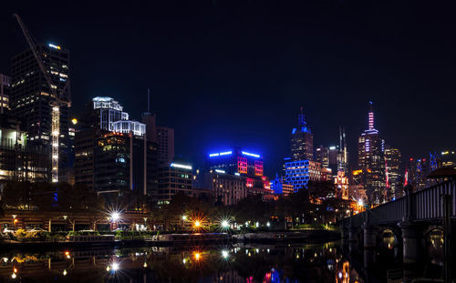 Illuminated buildings by river against sky at night