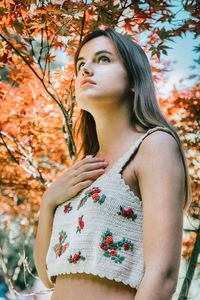 Young woman looking away while standing against trees during autumn