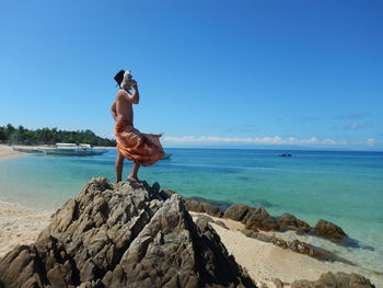 Rear view of shirtless man standing by sea against clear blue sky