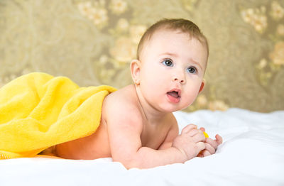 Curious baby girl under yellow towel lying on bed at home