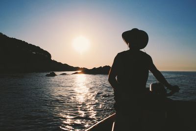 Silhouette man in boat on sea against sky during sunrise