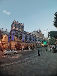 Cars on road by buildings in city against clear sky