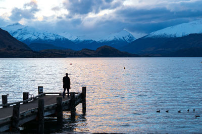 Silhouette man standing in lake against mountains during winter