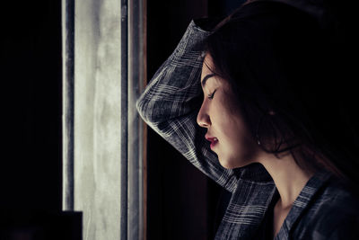 Close-up of young woman leaning on window at home