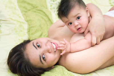 Portrait of shirtless woman with son lying on bed at home