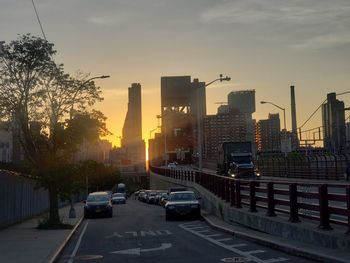 Cars on road by buildings against sky during sunset in city