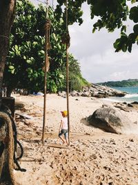 Full length of girl on beach by swing against sky