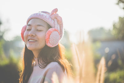 Smiling woman wearing hat and ear muffs during sunny day