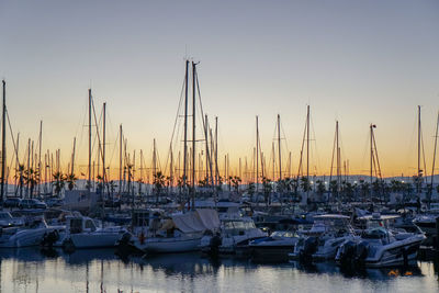 Sailboats moored in harbor at sunset