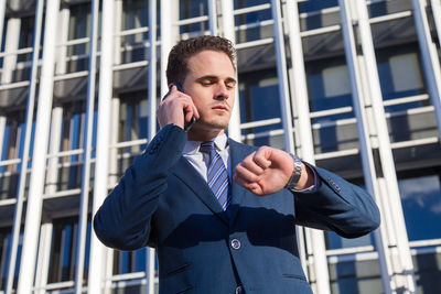 Low angle view of businessman talking on smart phone while standing against building